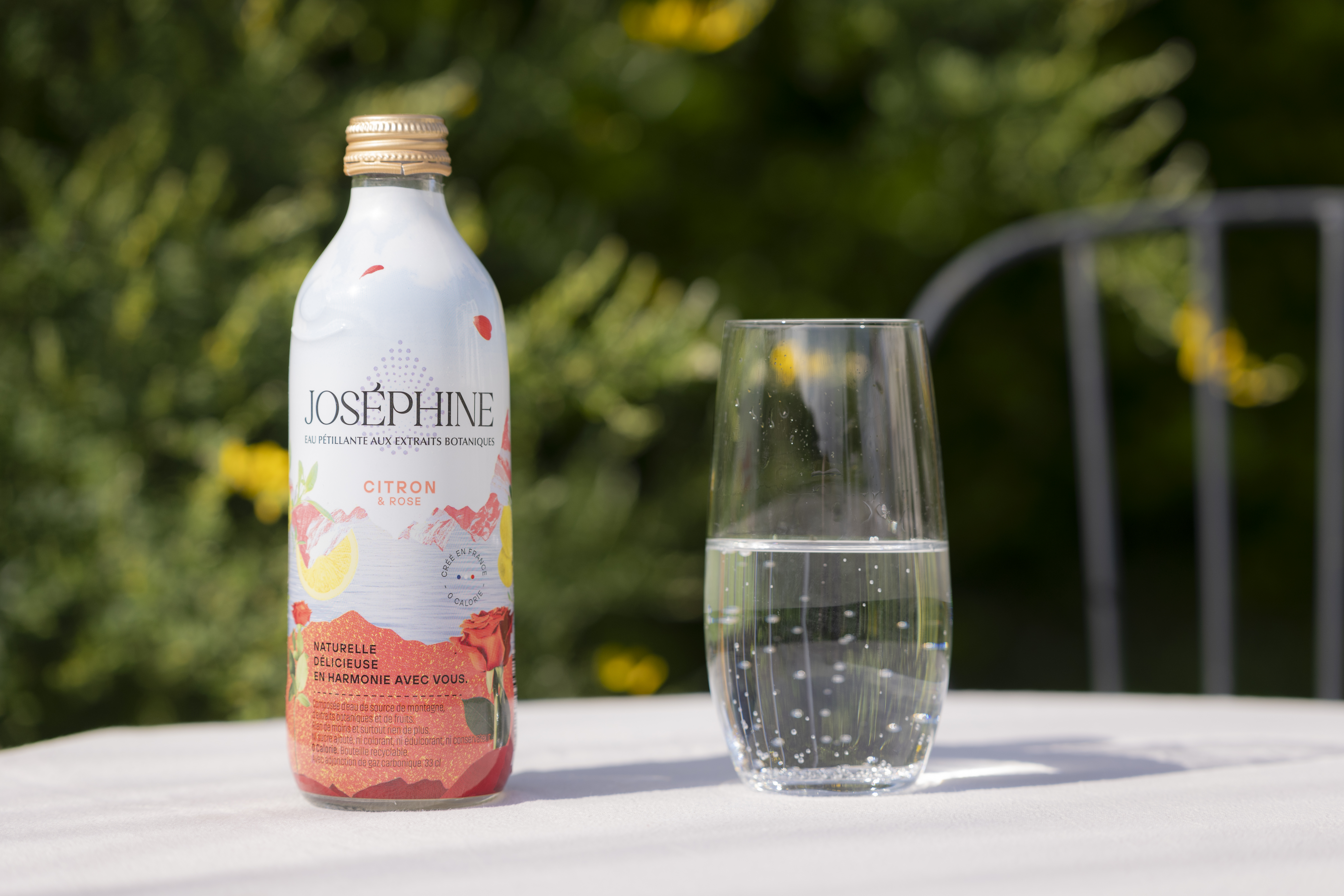 Bouteille Joséphine Citron & Rose avec un verre d’eau pétillante sur une table en extérieur